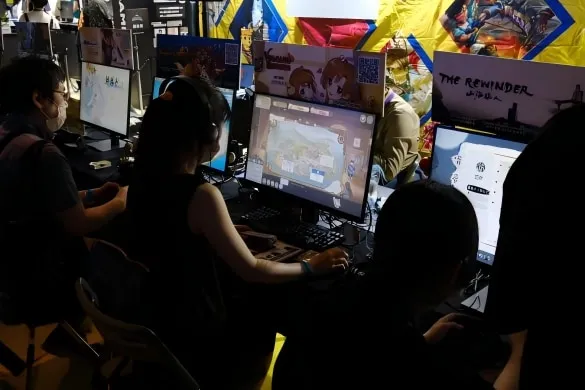 Visitors playing at a row of PCs in a shared independent games area of the show floor.